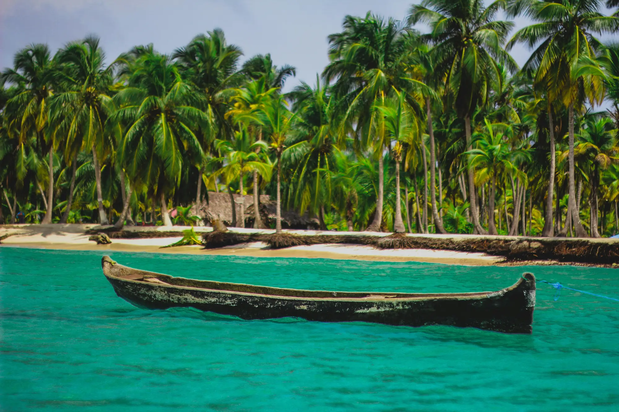 A dugout canoe on turquoise water by a sand spit with palms