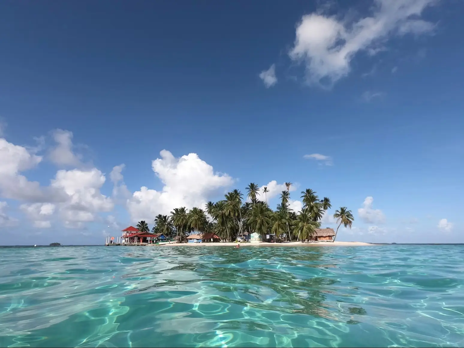 A tiny islet with palms and a jetty, seen from the water