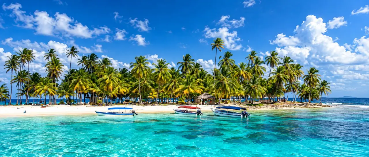 A low sand island in palms, boats under canopies on the shore