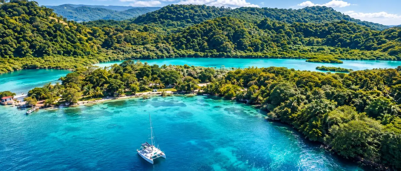 A sheltered bay with wooded hills, a catamaran at anchor