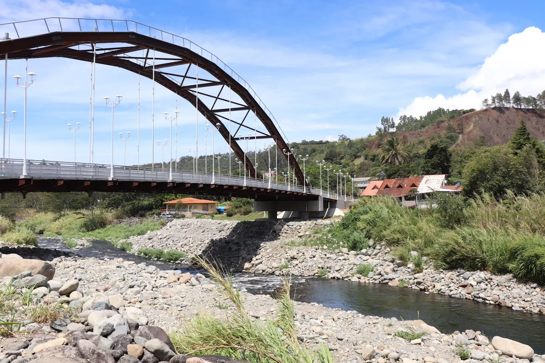 A steel arch bridge across the wide stony bed of a mountain river