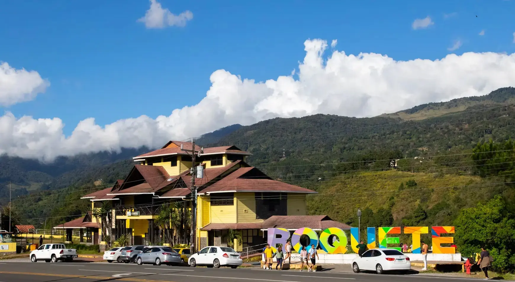 BOQUETE letters by the road, a yellow building with a tiled roof and a wooded slope behind it