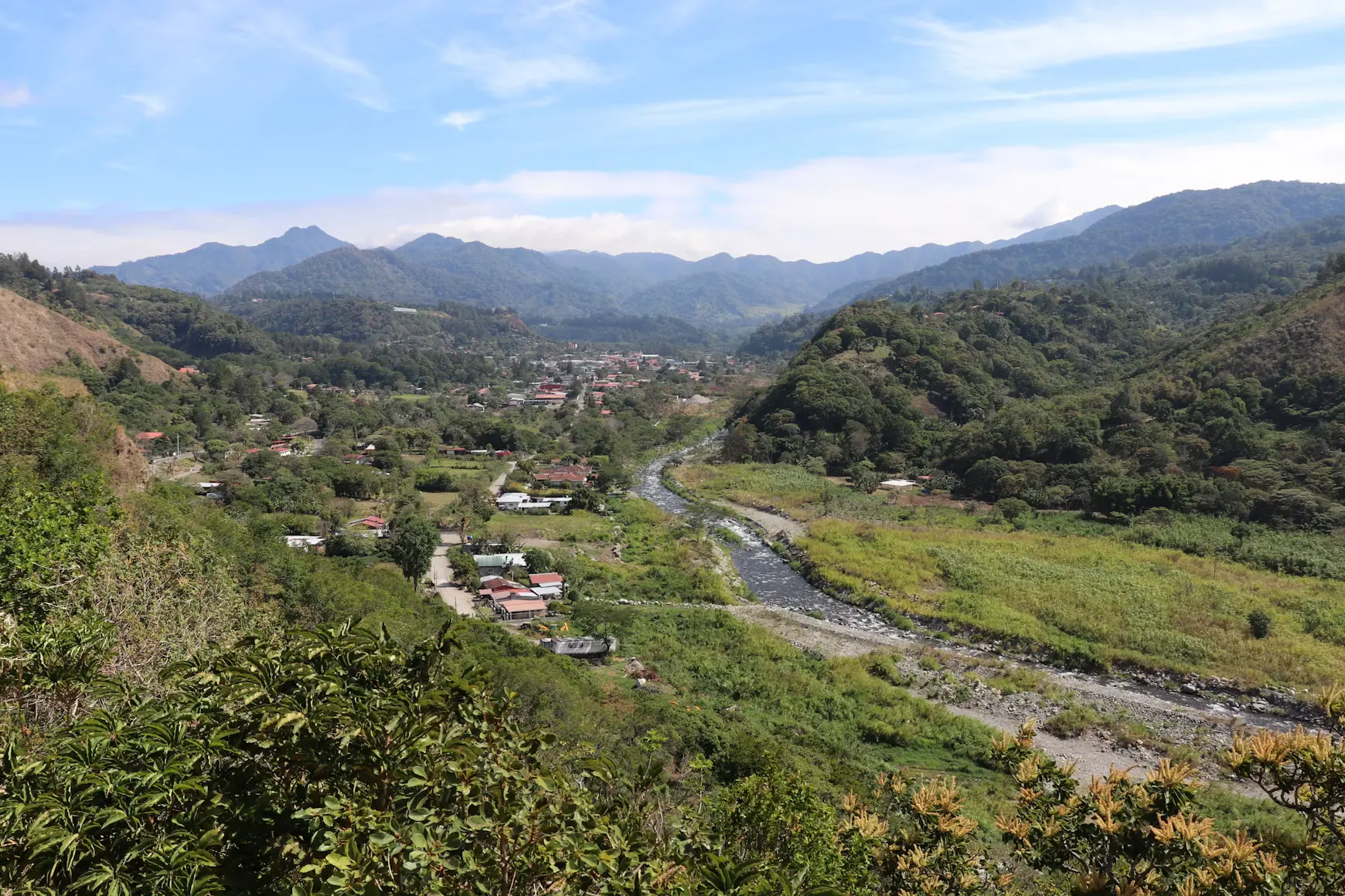 A view from above down a river valley towards a town, a stony bed among pasture