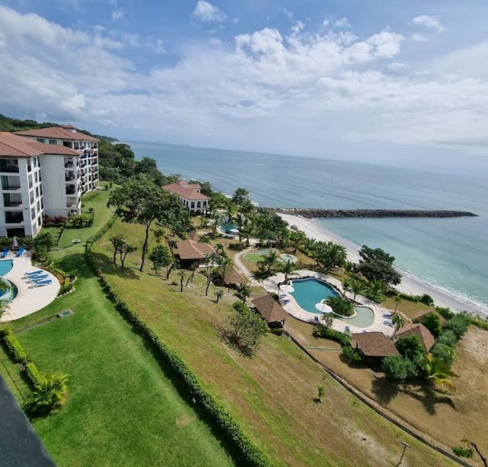 From above: blocks with terraces, lawns and two pools, a beach with a rock groyne below