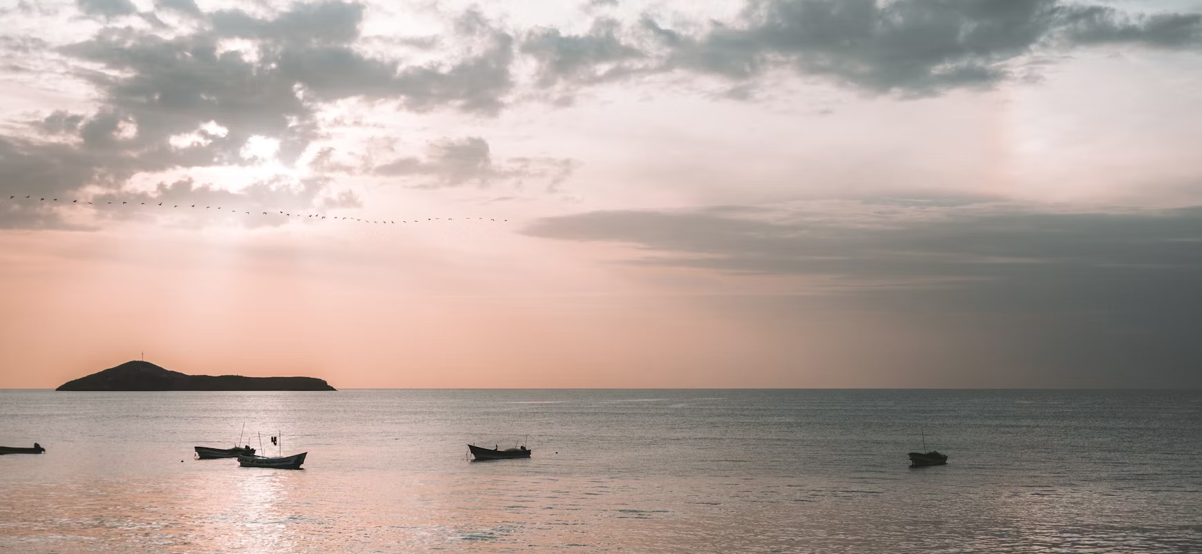 Small fishing boats on calm water in pre-dawn light, a low island in the distance