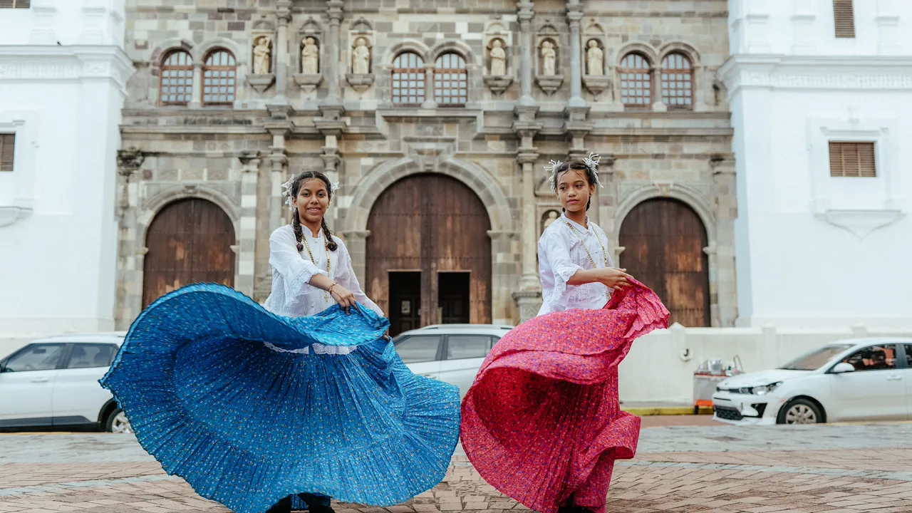 Two young women in polleras twirling on a square in front of a cathedral